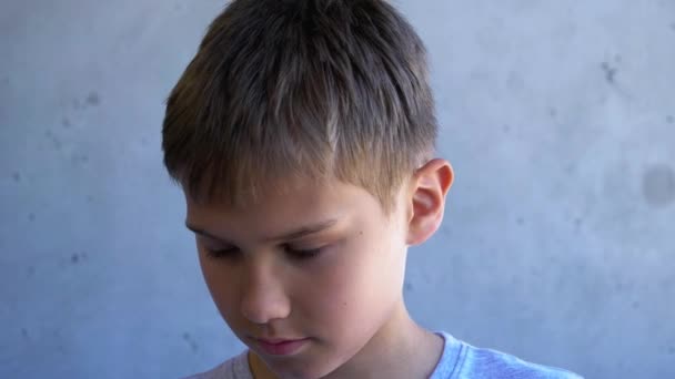 Portré tini fiú felemeli lehajtott fejét, és néz oldalra. Gyerek áll a koszos szürke fal mellett — Stock videók