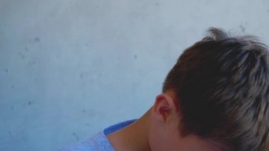 Sakin farkındalık genç çocuk başını kaldırır ve kameraya bakar. Gri duvarın yanında duran çocuk.