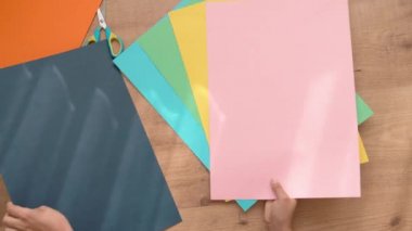 Elinde renkli kağıtlar olan çocuk evde sanat ödevi yapmaya başlıyor. Yukarıdan aşağıya doğru. 4k video