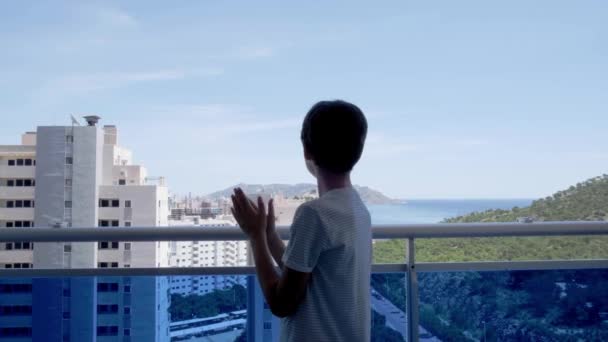 Junge klatscht in die Hände, winkt, grüßt mit Nachbarn. Applaus vom Balkon zur Unterstützung von Ärzten, Krankenschwestern und Krankenhauspersonal in Spanien während der Quarantäne vor der Coronavirus-Pandemie — Stockvideo