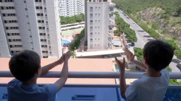 Jongens klappen met handen, zwaaien met de hand, groeten met buren. Van balkon naar balkon om artsen, verpleegkundigen, ziekenhuispersoneel in Spanje te ondersteunen tijdens de Coronavirus pandemie quarantaine — Stockvideo