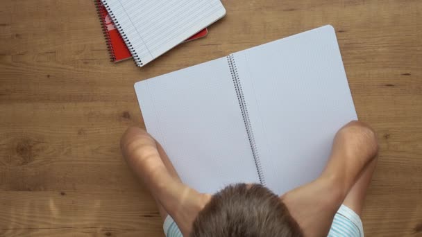 Kid sitting at table with open notebooks and lowered his had on the hands. Education, learning difficulties, school homework, learning at home — Stock Video