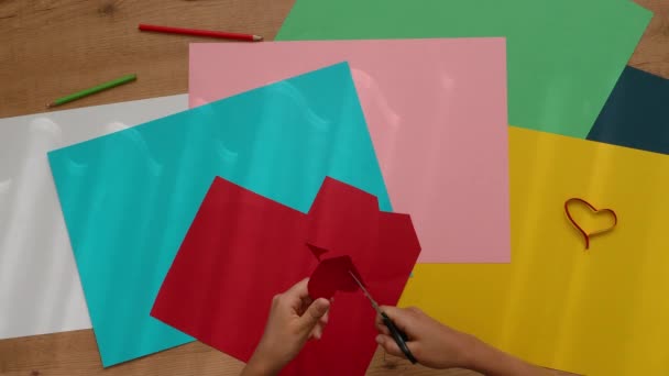 Детские руки режут ножницами цветную бумагу. Вид сверху вниз на стол с цветной бумагой. Обучение, ремесло, искусство для детей — стоковое видео