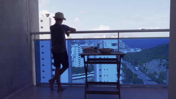 Junge steht auf Balkon, schaut sich um, isst frische Kirschen und genießt sonnigen Sommertag — Stockvideo