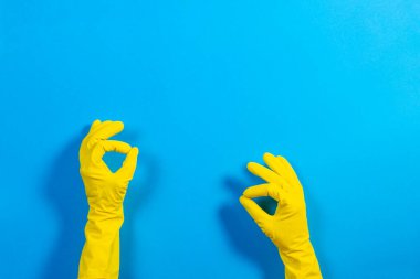 Sarı lastik eldivenli kadın elleri jest yapıyor. Tamam, mavi arka planda üst manzara.