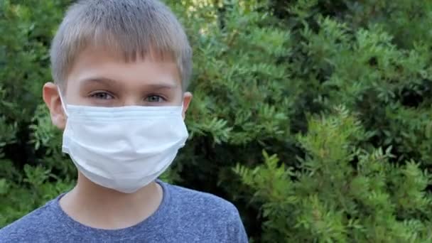 Chlapec s lékařskou ochrannou maskou dívající se do kamery. Dítě stojící venku — Stock video