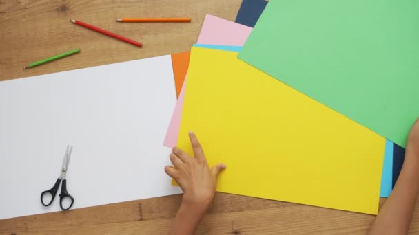 As mãos de criança escolhem que papel colorido usar no novo projeto de escola. Aprendizagem, artesanato, arte para crianças. Visão de cima para baixo — Vídeo de Stock