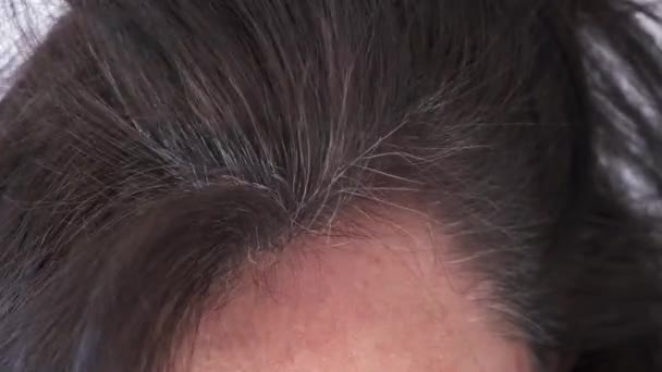 Mujer de mediana edad tocando su cabello oscuro con canas en las raíces del cabello — Vídeo de stock