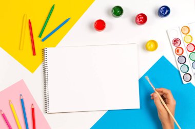 Öğrenme, hobi, sanat geçmişi. Çocuk çizim defterinin üzerinde resim malzemeleriyle el resmi yapıyor. Üst görünüm
