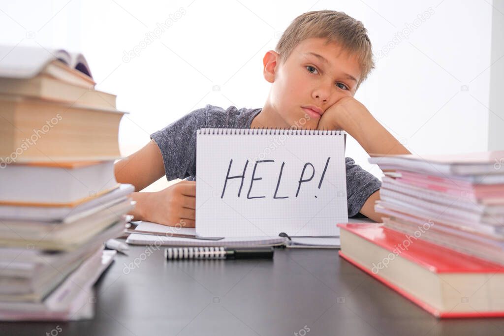 Learning difficulties, school, quarantine education concept. Tired frustrated boy sitting at table with many books. Word Help on open notebook.