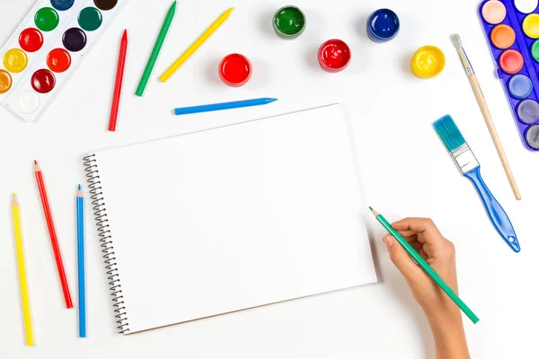 색칠 된 연필로 그림을 그리는 아이는 미술 도구들이 사방에 있는 스케치북 위에 손을 그립니다. 학습, 취미, 예술적 배경. 위에서 본 풍경 — 스톡 사진