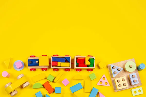 Bebek çocukların oyuncak geçmişi. Ahşap tren, eğitici renk tanıma oyuncağı ve sarı arka planda renkli bloklar. Üst görünüm — Stok fotoğraf