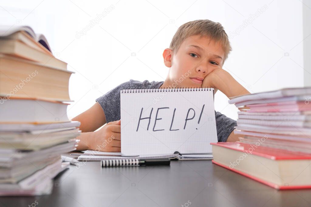 Learning difficulties, school, quarantine education concept. Tired frustrated boy sitting at table with many books. Word Help on open notebook.