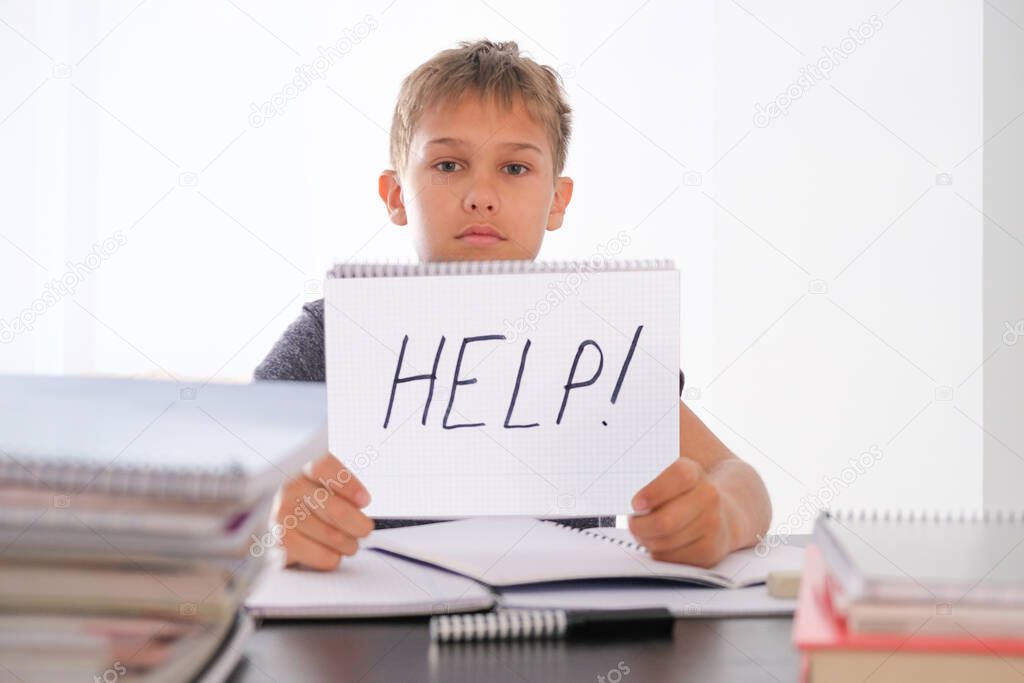 Learning difficulties, school, quarantine education concept. Tired disappointed boy sitting at table with many books. Word Help written on notebook