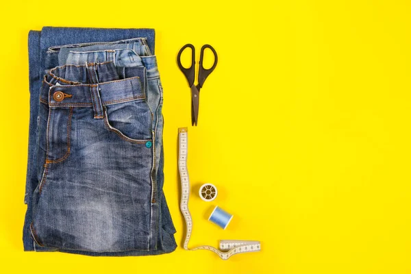 Staré modré džíny připravené k recyklaci v oběhovém hospodářství. Šicí nástroje a nůžky na žlutém pozadí. Horní pohled — Stock fotografie