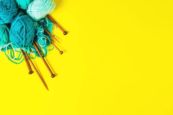 Knitting needles and knitting wool in light blue and green colors on yellow background. Top view — Stock Photo, Image