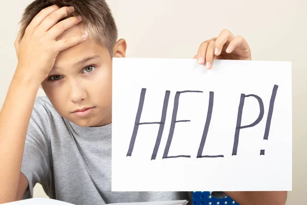 Dificuldades de aprendizagem, escola, educação, conceito de aprendizagem remota online. Miúdo triste sentado à mesa com computador portátil e cartão de segurança com palavra Ajuda — Fotografia de Stock