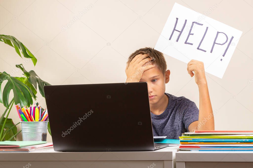 Learning difficulties, school, education, online remote learning concept. Sad kid sitting at table with laptop computer and holding card with Help word