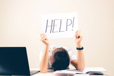 Öğrenme güçlüğü, okul, eğitim, çevrimiçi uzaktan öğrenme kavramı. Dizüstü bilgisayarı olan üzgün çocuk yardım sözcüğüyle kart tutuyor.