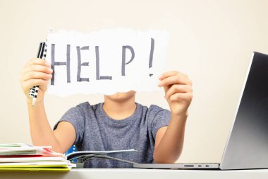 Öğrenme güçlüğü, okul, eğitim, çevrimiçi uzaktan öğrenme kavramı. Üzgün çocuk dizüstü bilgisayarla masada oturuyor ve elinde yardım sözcüğüyle kart tutuyor.