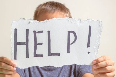 Öğrenme güçlüğü, okul, eğitim, çevrimiçi uzaktan öğrenme kavramı. Üzgün çocuk dizüstü bilgisayarla masada oturuyor ve elinde yardım sözcüğüyle kart tutuyor.