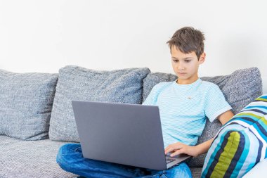 Evde dizüstü bilgisayar kullanan bir çocuk. Teknoloji, çevrimiçi öğrenim, uzaktan eğitim, ev ödevi, çocuklar için eğitim oyunları
