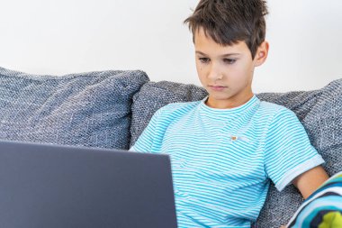 Evde dizüstü bilgisayar kullanan bir çocuk. Teknoloji, çevrimiçi öğrenim, uzaktan eğitim, ev ödevi, çocuklar için eğitim oyunları