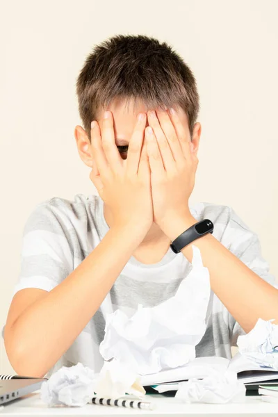 Kind bedeckt sein Gesicht mit den Händen und lugt mit einem Auge zwischen den Fingern hervor. Trauriger Junge hat Lernproblem bei Hausaufgaben — Stockfoto