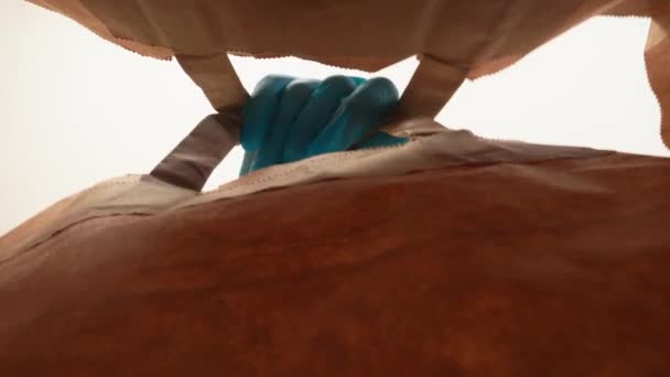 Woman with medical protective mask and latex gloves carefully opens paper shopping bag delivery from online store. Low angle view — Stock Video