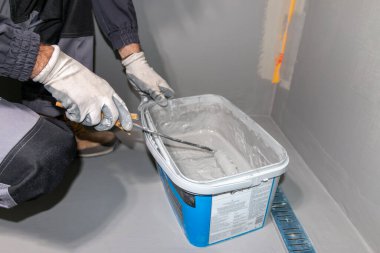 A builder worker applying waterproofing paint to the bathroom wall and floor. Applying waterproofing in the bathroom. clipart