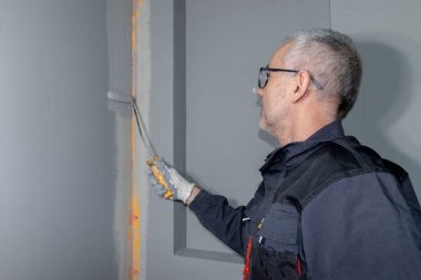 A builder worker applying waterproofing paint to the bathroom wall and floor. Applying waterproofing in the bathroom. clipart