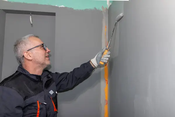 Banyo duvarına ve yere su geçirmez boya uygulayan bir inşaat işçisi. Banyoya su yalıtımı uyguluyorum..