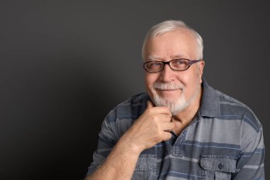 Yetişkin, beyaz saçlı, gözlüklü bir adam iyi niyetle gülümsüyor.