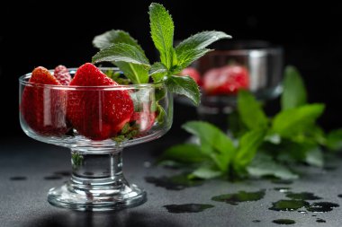 Siyah arka planda cam bir kasede taze olgun kırmızı çilekler.