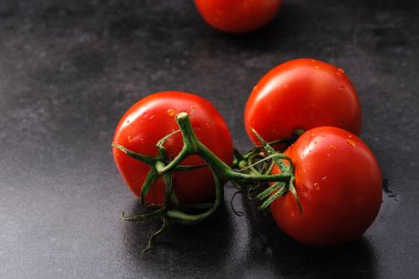 Su damlaları olan bir dalda kırmızı olgun domatesler gri bir arka planda uzanır, taze sebzeler.