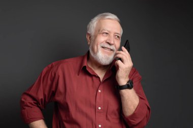 business-haired, gray-haired man in a red shirt is talking to the phone and laughing on a gray background clipart