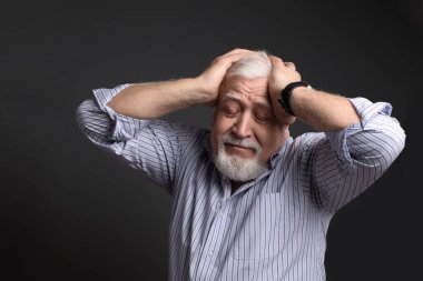 İş adamı saçı olan bir adam iki elini başının üstüne koydu ve gözleri gri arka planda kaldı.