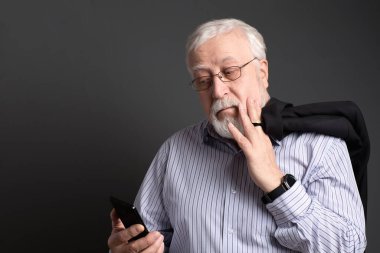 İş adamı, beyaz saçlı, gözlüklü, gri arka planda telefonu olan adam güler yüzlü, dost canlısı.