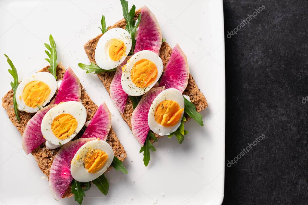 Colorful sandwiches of cereal bread with boiled eggs with radish and arugula