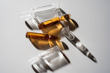 Çeşitli cam ampulleri, nötr yüzeydeki yumuşak ışıkla aydınlatılan temiz ve kehribar sıvı formları sergiler.