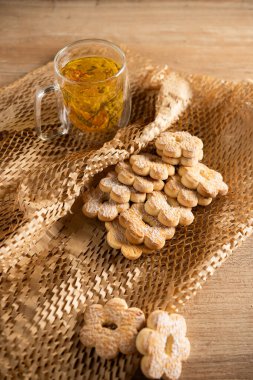 Sıcak öğleden sonra ışığında bir fincan bitkisel çayın yanına sade bir masaya yerleştirilmiş lezzetli kurabiyeler.