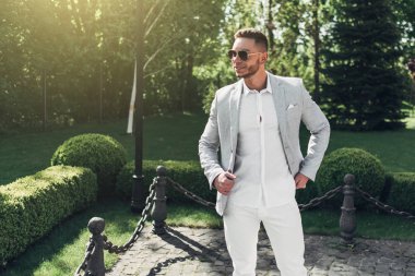 Sakallı ve güneş ışığı altında sokakta şık takım elbise poz içinde gözlüklü genç adam