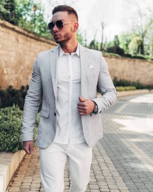 Sakallı ve güneş ışığı altında sokakta şık takım elbise poz içinde gözlüklü genç adam