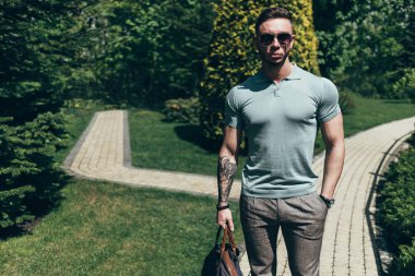 Sakallı ve güneş ışığı altında sokakta şık kıyafet poz içinde gözlüklü genç adam