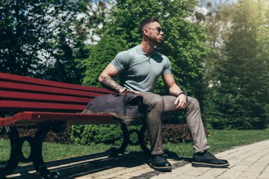 Sakallı ve güneş ışığı altında sokakta şık kıyafet poz içinde gözlüklü genç adam