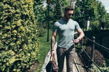 Sakallı ve güneş ışığı altında sokakta şık kıyafet poz içinde gözlüklü genç adam