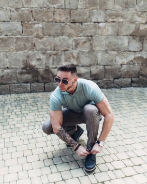 Sakallı ve güneş ışığı altında sokakta şık kıyafet poz içinde gözlüklü genç adam