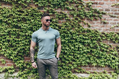 Sakallı ve güneş ışığı altında sokakta şık kıyafet poz içinde gözlüklü genç adam