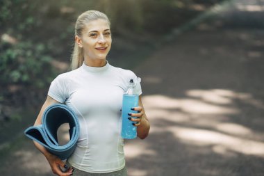 Fitness kadın erken sabah parkta Yoga için hazırlanıyor. Şık spor kıyafeti giymiş. Mavi şişe su ve Yoga Mat. Sağlıklı yaşam tarzı.