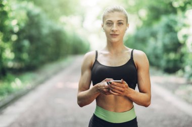 Smartphone cep telefonu ile Bluetooth kulaklık kullanarak müzik dinlemek kadın Runner yaz sabah parkta. Kadın kız dışında yolda koşu.